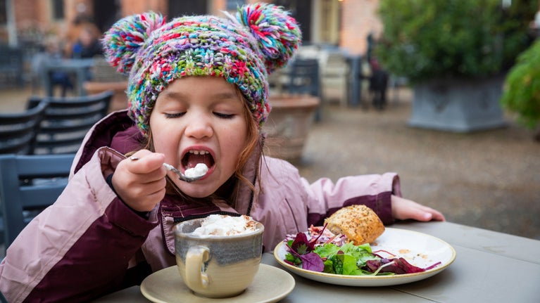 Child enjoys a hot chocolate and sausage roll outside the Squire's Pantry tea-room at Felbrigg Hall, Gardens and Estate Norfolk.